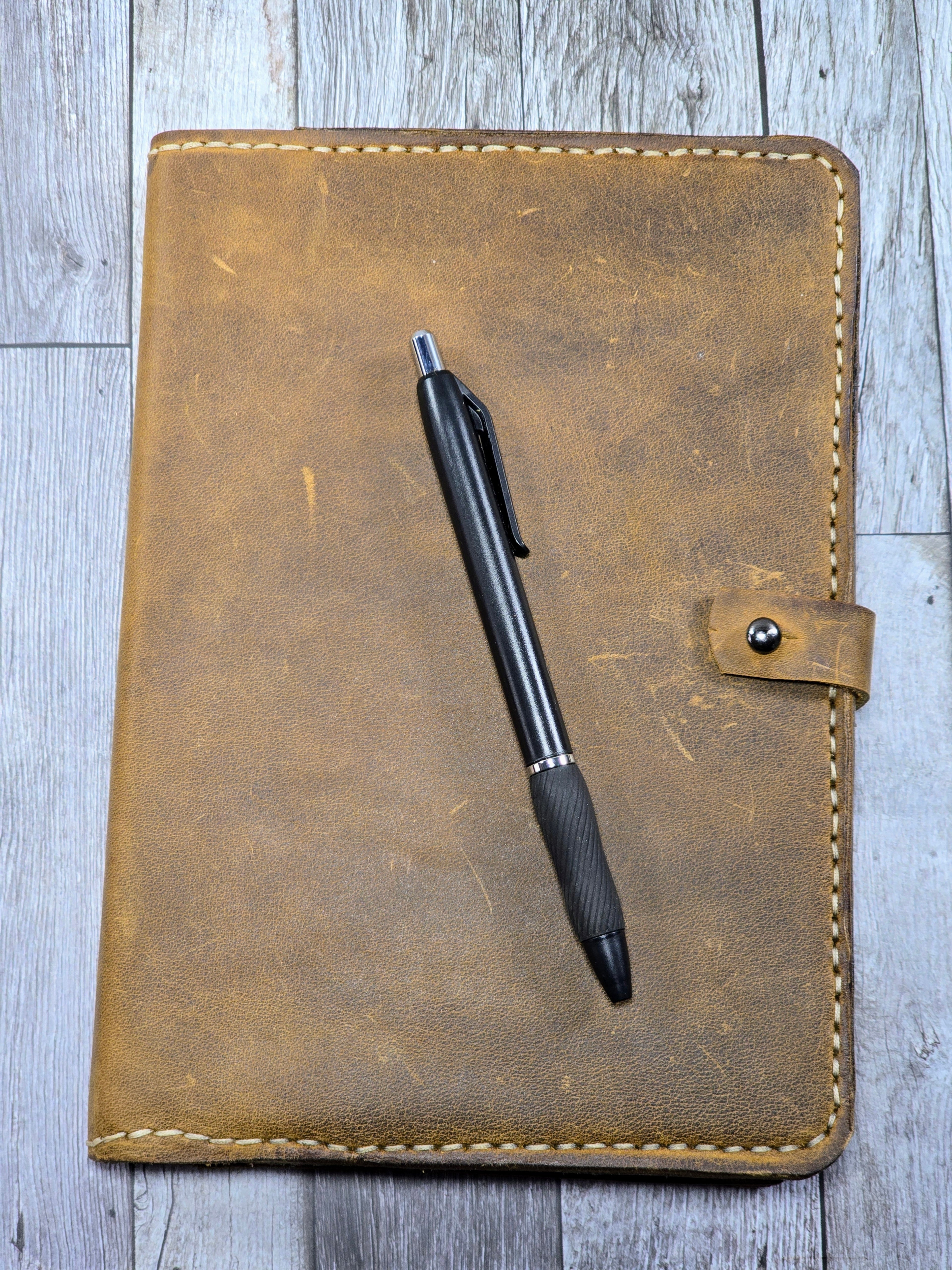 Brown leather journal cover with a pen on a wooden surface 