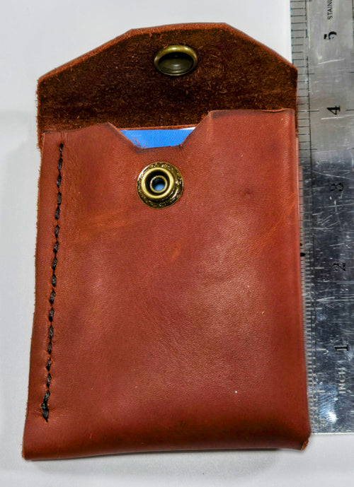 Burgundy leather minimalist with an antique brass snap on a white background and a ruler to show size