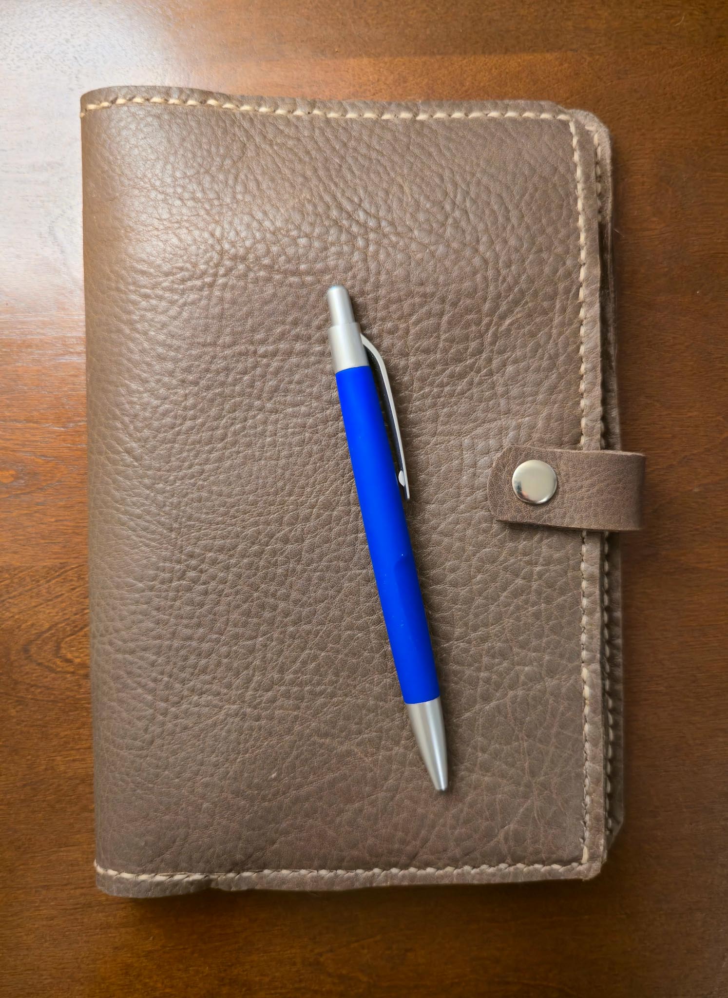 Brown leather mini padfolio with a blue pen on a wooden surface