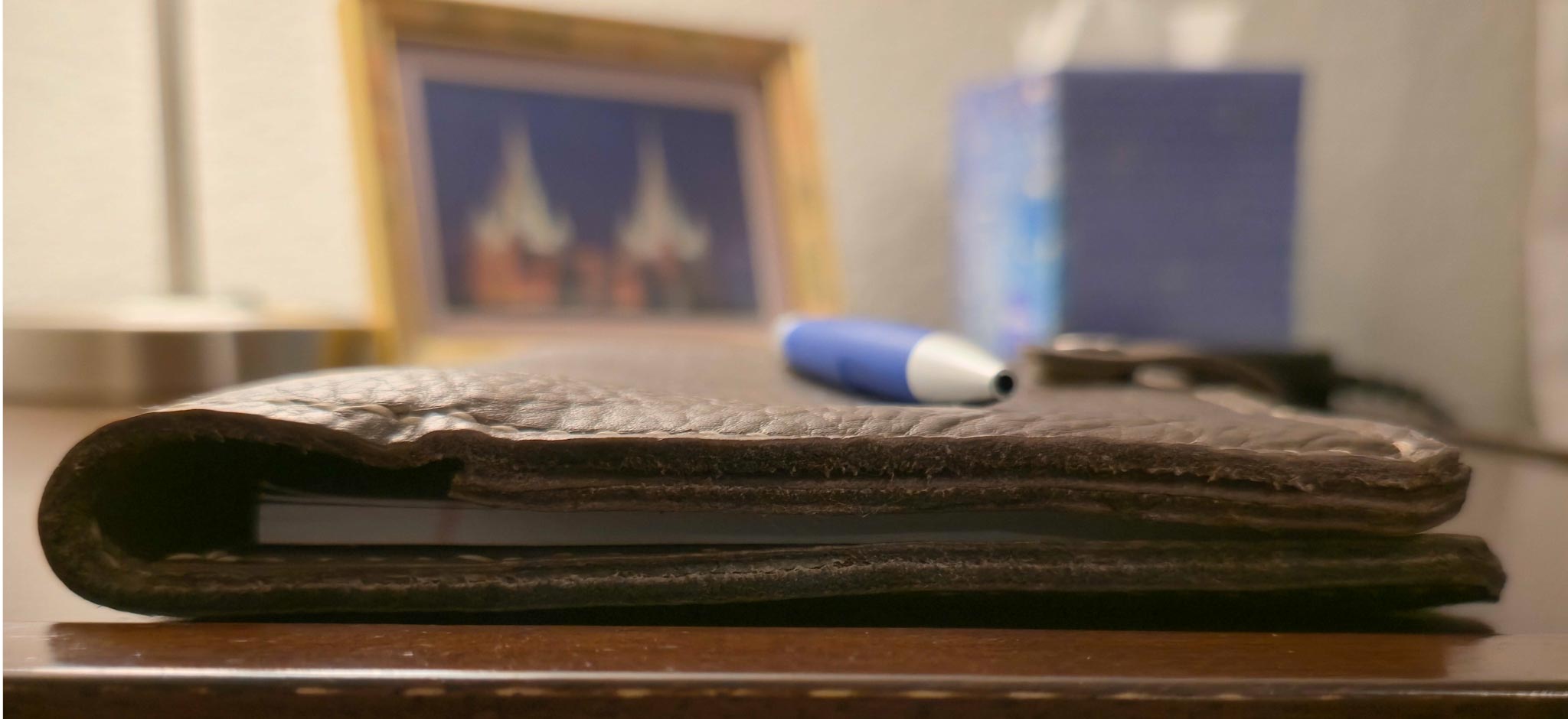 Side view of Brown embossed leather mini padfolio on a wooden surface with a blurred background
