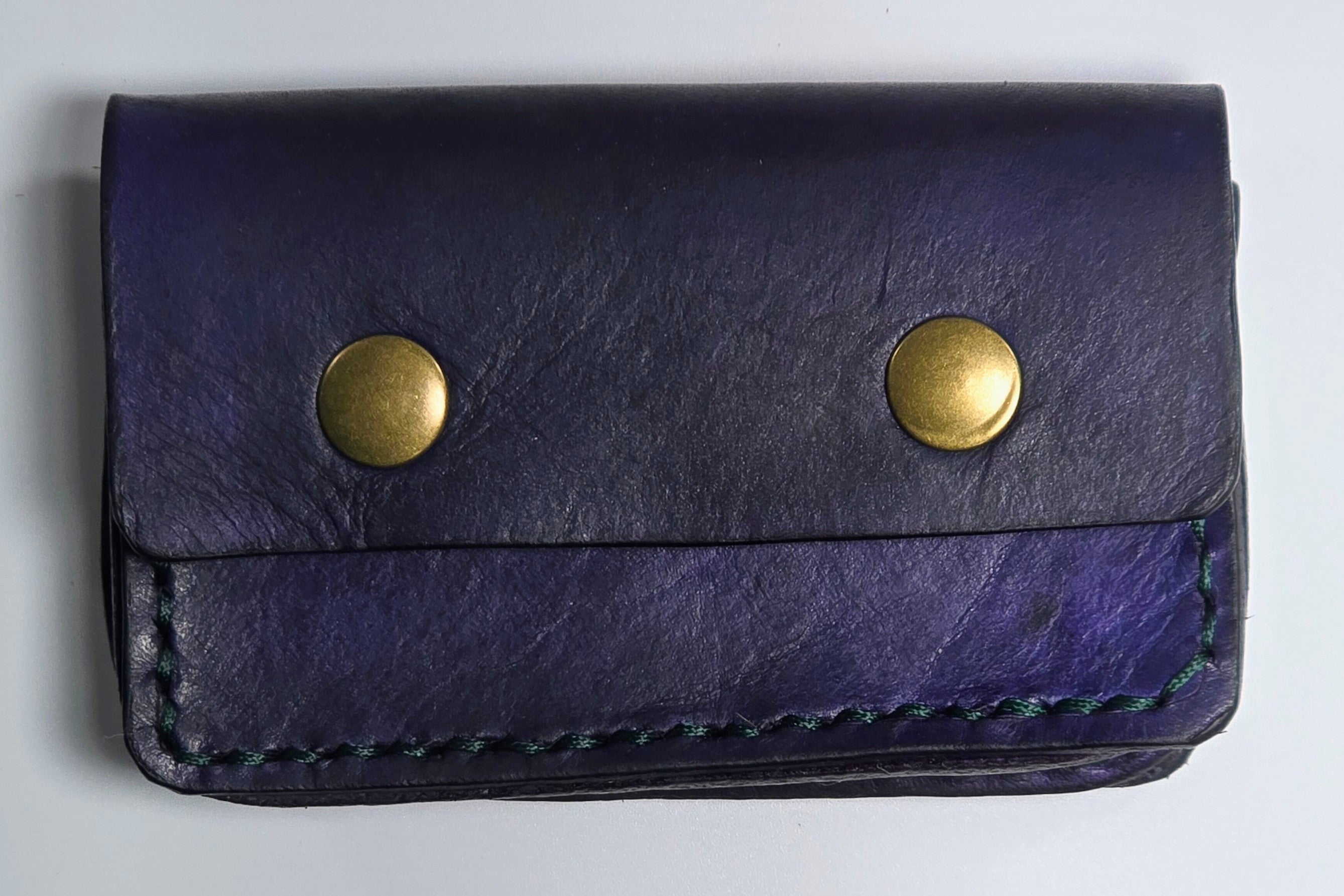 Navy leather card wallet with brass magnetic snaps on a light gray background