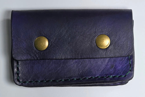 Navy leather card wallet with brass magnetic snaps on a light gray background