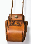 A brown leather crossbody bag with a hand-tooled western design on the front flap, a brass snap button, and a long leather strap, shown against a plain white background.